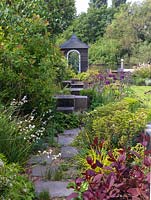 Riverside garden by Andy Sturgeon. Path leads past cotinus, euphorbia, libertia, carex. Oak cubes pass allium, erysimum, Hebe vernicosa, box, iris, aquilegia, fern.