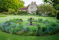 Formal garden in front of Grade II Jacobean manor house, with circular beds planted with verbascum, irises and forget-me-nots. King John's Nursery, Etchingham, East Sussex, UK