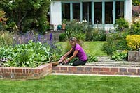 Nicola Stocken planting tobacco plants between stone strips in her newly rebuilt riverside garden, four months after it was devastated by flooding.