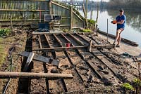 After weeks of flooding, a riverside deck has to be completely rebuilt. The first step is to remove the hardwood decking planks, revealing the softwood subframe which is rotting in parts because a build-up of wet mud has been deposited between the joists.
