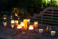 A table with candles and a backlit border illuminate a garden at night.