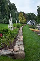 White Flower Farm front grounds with obelisks, half stone wall, tiered display beds, weeping beech and store in background.
