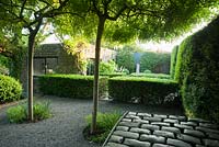 Courtyard with four trained weeping ash, Fraxinus excelsior 'Pendula' and steel and lead container inlaid with granite setts is surrounded by tall yew hedges