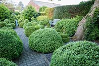 Topiary garden filled with low clipped box bushes a grey painted bench and chimney pot focal point. 
