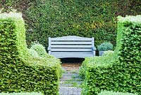 Grey painted bench in the topiary garden stencilled with the words Carpe Diem, framed by yew hedge and viewed from the kitchen garden.