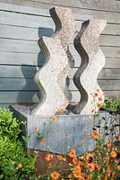 Cast concrete sculpture by Helen Sinclair in the flower garden surrounded by orange and purple geums and aquilegias. 