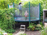 Isla and Romy bounce on the screened trampoline in a family friendly garden, Muswell Hill, London.