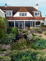 An exposed seaside garden is laid to shingle, with raised beds contained within driftwood, and planted with sea kale and quaking grass