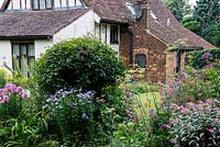 A mixed border at Southend Farm with asters, fennel, clematis and phlox in front of a medieval farmhouse.