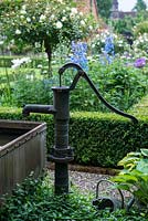 A decorative water pump beside a pond in a galvanised trough.