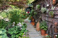 A town garden with narrow slab path besides a painted garage decorated with salvaged garden tools and hanging containers.
