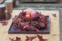 Wreath of Sedum - stonecrop and Rosa - rose hips on wooden coasters, silver bowl with candles in the middle, red autumn leaves
