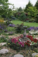 View of country garden sundial set on small raised bed circular stepping stones set in gravel. 