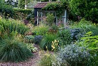 A summer house in a grass and perennial gravel garden. Planting includes Stipa gigantea, Eryngium Tetra Blau, Verbascum Aztec Gold and Selinium wallichianum.
