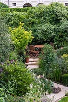 A town garden with secluded seating area surrounded by dense mixed borders.