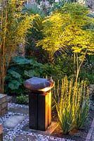 Lit at night, ceramic bird bath by Sarah Walton, edged in sisyrinchium and euphorbia. Behind, yellow bamboo, umbrella plant, royal fern, Chusan palm, phormium and maple.