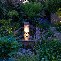 Lit at night,  long pool edged in hostas, lavender, Hakonechloa macra, Persicaria bistorta Superba, Iris sibirica 'Caesar's Brother' and male ferns. Pond sculpture by Peter Hayes.