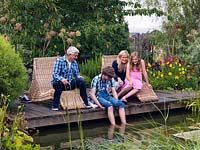 Joanne and Graham Winn with their children Sebastian and Scarlet relaxing on the pond side deck. Surrounding plants include Verbena, Helenium and Angelica gigas.