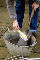 Woman cleaning garden spade with brush, rinsing with water, November