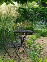 Gravel garden with metal furniture viewed through pleached hornbeam hedge. Perennials include Verbena bonariensis and Stipa gigantea.