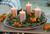 Mediterranean Advent display with fruits of Calamondin Oranges - Citrofortunella, vines of clematis, Pinus, black dates, and cream-colored candles, mandarin oranges studded with cloves