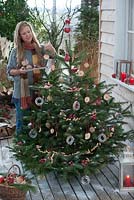 Christmas tree on terrace - woman decorating Abies nordmanniana used as a birdseed tree with apple slices, peanuts and cereal 