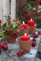 Terracotta pots used as candle holders decorated with Gaultheria procumbens and crabapples
