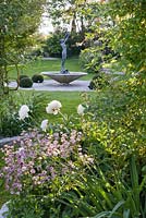 Water feature with woman statue. Astrantia major with honeybee and peony.