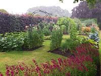 Potager. Metal tunnels, clad in sweet peas or runner beans, run down the centre of a formal scheme of beds filled with vegetables and flowers. Obelisks of sweet peas.