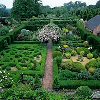 First floor view of Rose Arbour in centre of Gertrude Jekyll, Silver Pear, Gravel and Knot gardens. Pleached lime alley and Fountain Garden beyond. Rural, wooded landscape.