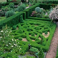 First floor view of knot garden created in clipped box hedges, balls and pyramids on gravel. Set against yew hedge and edged in reclaimed brick paths.