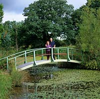 Chris and Sheila Bissell on the bridge spanning a spring-fed, 14 feet deep lake planted with  native water lilies. Inspiration from Monets bridge.