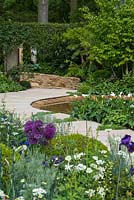 The Time In Between by Husqvarna and Gardena.  View over bed of allium, aquilegia, anchusa, geranium and box balls to pool edged in curving stone path and sunken seating area. 