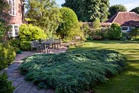 Path along Juniperus to patio with garden furniture at Hambledon House Hampshire.