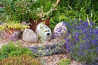 Decorative clay heads in gravel garden with Lavandula 'Hidcote' and Fuchsia 'Chequerboard', Helichrysum petiolare 'Limelight' in pots