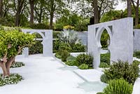 View of part of the garden with white marble paving, including Islamic archways and walls acting as dividers. Feature plants include Bismarckia nobilis at the back, Citrus aurantium in front, Myrtus sp., Rosmarinus officinalis, Salvia officinalis. Beauty of Islam. RHS Chelsea Flower Show, 2015