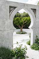 view of Citrus nobilis trees surrounded by Thymus vulgaris white and water feature through arabic style arch marble wall with white gravel path. The Beauty of Islam. Chelsea Flower Show 2015