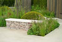 Drystone wall seat and stone terrace with clipped dome of Taxus baccata, grasses and perennials including Deschampsia flexuosa, Baptisia 'Dutch Chocolate', Astrantia 'Hadspen Blood' - RHS Chelsea Flower Show 2015