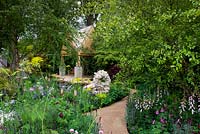 The M and G Garden - The Retreat, View down winding path to oak-framed garden building with stone sculpture. Cottage-style planting with roses and foxgloves. 