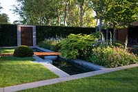 The Homebase Garden - Urban Retreat, view of modern pond surrounded by concrete blocks, corten steel wall and flowerbeds with Digitalis 'Pam's Choice', Geum 'Marmalade', Geum 'Totally Tangerine', Geranium sylvatica 'Mayflower' and Iris sibirica and topiary Taxus Baccata Ball 