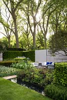 The Telegraph Garden, view of the patio with modern furniture surrounded by planting boxes with Osmanthus x burkwoodii, Achillea filipendulina 'Cloth of Gold', Paeonia Bartzella