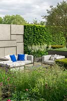Within beds of perennials, grasses and yew blocks, a  sunken seating area is backed by a wall and hornbeam hedge.  The Telegraph Garden. RHS Chelsea Flower Show 2015