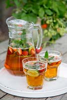 Two drinks of Pimm's and lemonade with Mint, Cucumber and Strawberries added to the jug