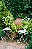 White metalwork chairs in front of urn. Also Phyllostachys bamboo and ferns inc. Athyrium filix-femina -lady fern and Asplenium scolopendrium - hart's tongue fern