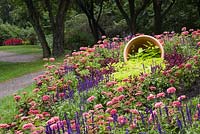 Terracotta flower pot with cascading green leaf plants, pink Zinnia and Salvia - Blue Sage flowers in border in public garden in summer, Centre de la Nature public garden, Saint-Vincent-de-Paul, Laval, Quebec, Canada
