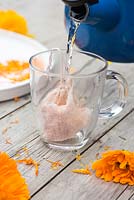 Adding boiling water to a cotton tea bag containing dried Calendula officinalis 'Art Shades' petals