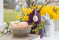 Floral display containing decorative eggs, Daffodils, Blossoming spring foliage and a Bunny, with a view to the garden