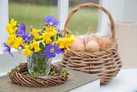 Floral display of Daffodils and Anemone, with a basket of eggs and a view to the garden