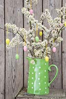 Decorative eggs hanging from blossoming spring foliage, in a green polkadot jug