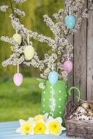 Decorative eggs hanging from blossoming spring foliage in a green polkadot jug, accompanied with Daffodils and Quail eggs